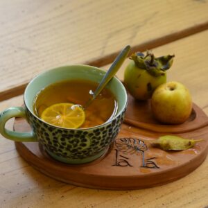 trà kombucha dưỡng nhan - Một tách trà thảo mộc ấm với chanh, được phục vụ kèm táo và hồng trên khay gỗ.