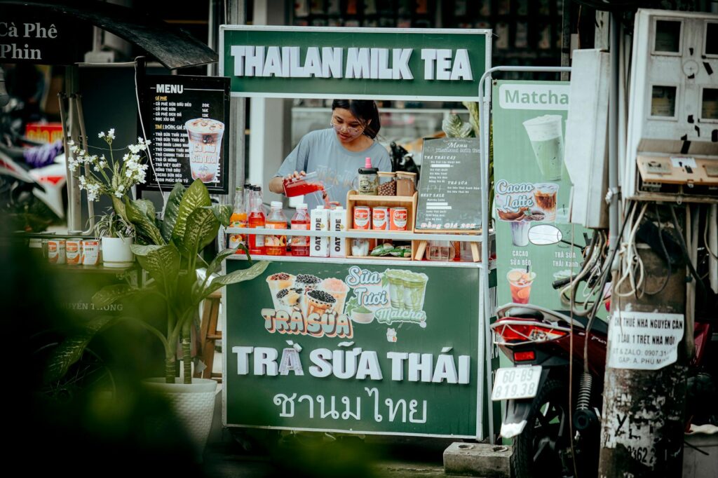 bí quyết nấu trà đá kinh doanh - Người bán hàng đang pha chế đồ uống tại một quầy trà sữa Thái ở ngoài trời.