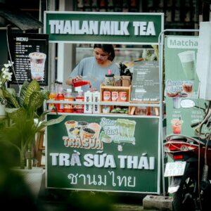 bí quyết nấu trà đá kinh doanh - Người bán hàng đang pha chế đồ uống tại một quầy trà sữa Thái ở ngoài trời.