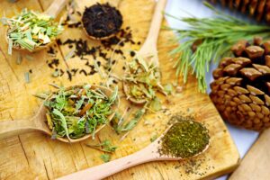 trà kết hợp siêu thực phẩm - Nhiều loại trà thảo mộc được trưng bày trên những chiếc thìa gỗ, đặt trên một tấm ván gỗ mộc mạc có quả thông.